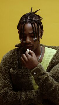 A young stylish black man on yellow background playing with chewing gum