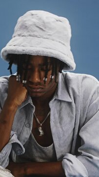 a young stylish black man answering and chatting on an old retro grey phone, sitting at a blue desk with a blue background, dressed all in grey with a furry hat