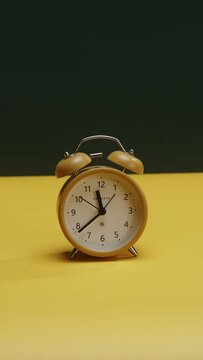 A yellow clock on a table, ticking, yellow and green background