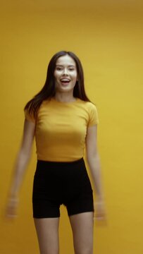 A young Asian woman, suddenly appearing on screen, smiling and waving hello