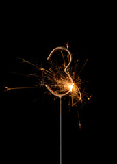 Burning golden sparkler in shape of number three, digit 3, isolated on black background