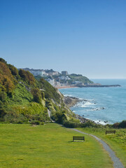 Sunlit, rugged coastline at Ventnor, with waves rolling in passed the headland to the beach and its terraced hotels.