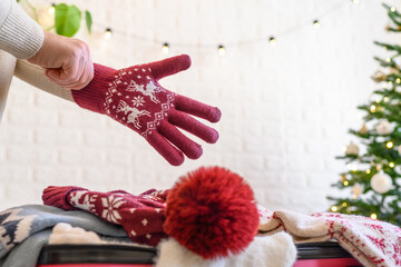 Christmas time. Woman putting knitted winter clothing in a suitcase in the room decorated christmas...