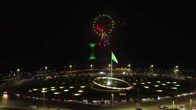 Aerial circling Saudi Arabian flag fluttering, fireworks night, Khobar Tower in background