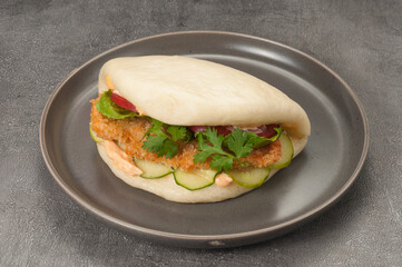 bao bun with breaded chicken and vegetables on a gray plate