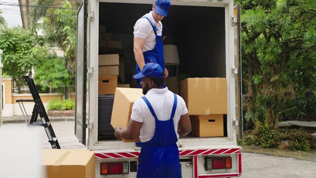 Workers unloading boxes from van outdoors.House move, mover service and Moving service concept.Two young handsome smiling workers wearing uniforms are unloading the van full of boxes.