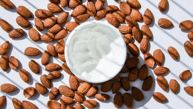 4k zoom in out jar with facial or body almond moisturizer jar open with almonds on the table. Top view. Horizontal composition, almond cream for skin, natural cosmetics beauty concept