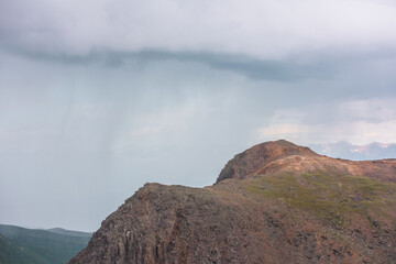 Dramatic aerial landscape with sunlit mountain top during rain at changeable weather. Atmospheric mountain scenery with sharp rocks in sunlight under lead gray cloudy sky. Rainy clouds in mountains.