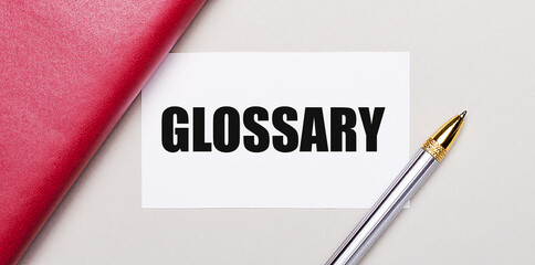 On a light gray background, there is a golden pen, a burgundy notebook and a white blank card with a place to insert text GLOSSARY. Business concept.
