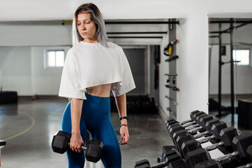 Sporty fitness girl is posing at the dumbbells in the gym