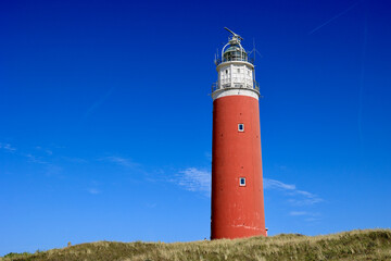 The lighthouse of the island of Texel in The Netherlands surrounded by tall sand dunes in beautiful...