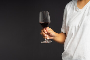 Close-up of hand holding a red wine glass while standing on a gray background