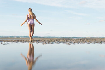 in a swimsuit image of a full length teenager girl posing from behind, enjoying the amazing ocean view, spinning and having fun, relaxing in freedom.