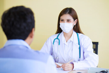 Asian woman doctor wears a medical face mask and records symptom of a man patient on paper in hospital.    Coronavirus protection concept.