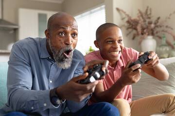 Happy african american male teenager with his father playing video games