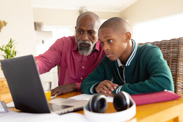 African american male teenager learning with his father and using laptop