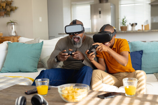Happy african american male teenager with his father playing video games and using vr headset