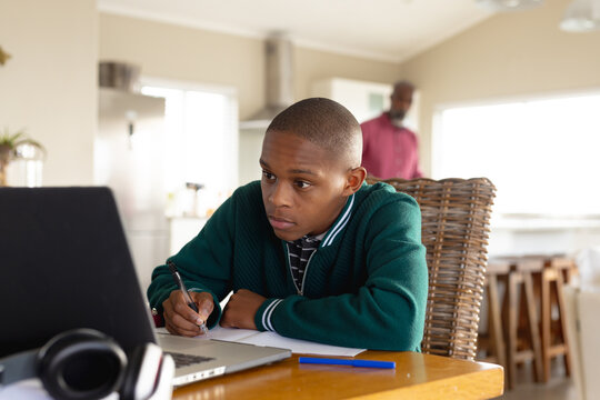 African american male teenager learning with his father and using laptop