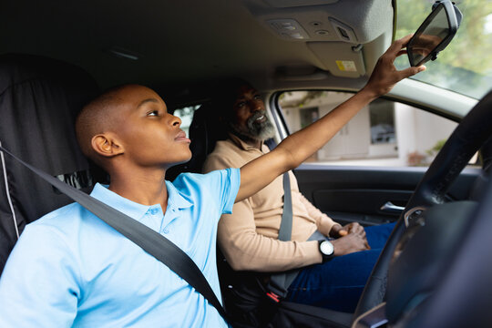 Happy african american male teenager driving car with his father