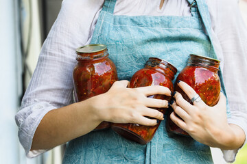 Woman's hands holding homemade canned quart mason jars of tomato salsa. Selective focus with blurred background. - obrazy, fototapety, plakaty