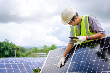 A male engineer in a white hard hat holds a tablet to inspect solar panels. At photovoltaic power stations working on industrial solar energy storage.