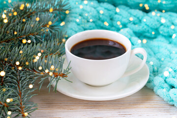 Obraz na płótnie Canvas A cup of coffee, a plaid, and a Christmas tree branch in blurry lights