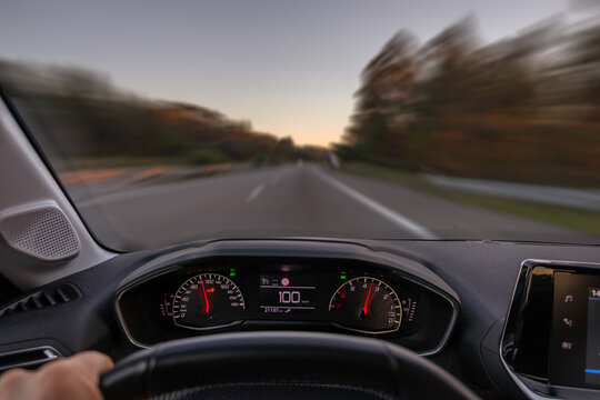 Driver view to the speedometer at 100 kmh or 100 mph and the road blurred in motion, night fall view from inside a car of driver POV of the road landscape.