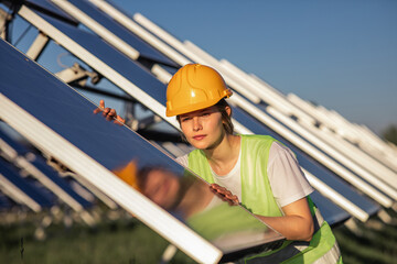 Pretty lady engineer assistant at photovoltaic solar farm she analysing the cleanliness of the photovoltaic solar panels she wearing safety equipment - obrazy, fototapety, plakaty