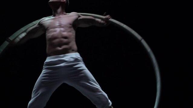 Muscular circus artist perform Cyr Wheel on a black background. Concept of willpower, motivation and passion