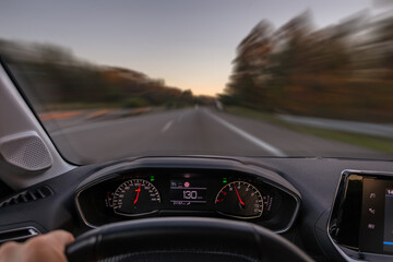 Driver view to the speedometer at 130 kmh or 130 mph and the road blurred in motion, night fall...