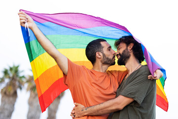 Gay couple embracing and showing their love with rainbow flag. LGBT community.