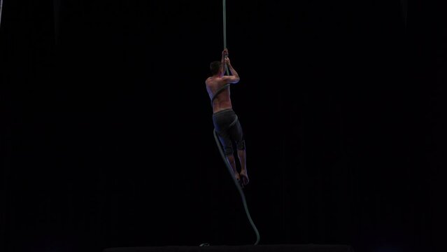 Muscular and fit circus artist perform on aerial rope on high altitude