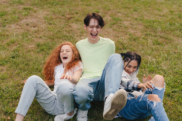 Three happy teenagers fell down on the grass while making a video to post on the internet. Funny...