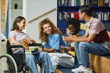 Diverse group of young people chatting in college library including female student with disability - obrazy, fototapety, plakaty