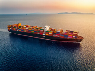 Aerial view of a large container cargo ship traveling over ocean into the sunset
