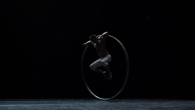 Muscular circus artist perform Cyr Wheel on a black background stage in slow motion