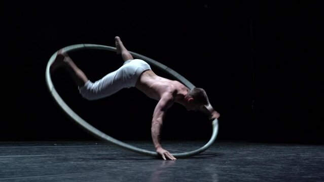 Muscular circus artist perform Cyr Wheel on a black background stage in slow motion