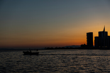 Fototapeta premium View of fishing boat with two fisherman gliding in the sea at sunset in Mavisehir, Karsiyaka, İzmir. Beautiful sunlight over skyline. Selective focus, noise effect and grainy texture.