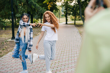 Two young and beautiful girls posing showing a heart made of fingers and giving high fives with their legs, outdoors. To share video to social media application