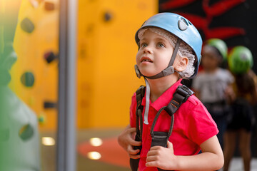 Cute little girl climber in blue protective helmet and gear for climbing standing in climber centre...