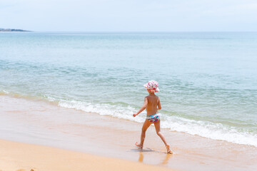 Back view of adorable little girl at sandy Atlantic ocean beach during summer