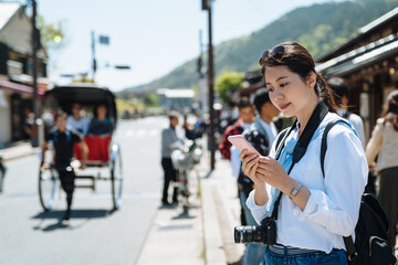 portrait of pretty Asian female visitor in japan is using mobile phone on the sidewalk at...