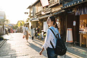 backlit photograph asian female backpacker is gazing into the distance with curiosity while walking down historic ninen zaka street at dusk in autumn Kyoto japan - obrazy, fototapety, plakaty