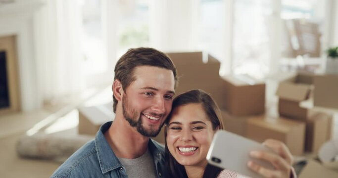 Happy couple taking a selfie with a phone in their new home apartment space or house on moving day. Man and woman real estate property owners with box in the background feeling proud in a living room