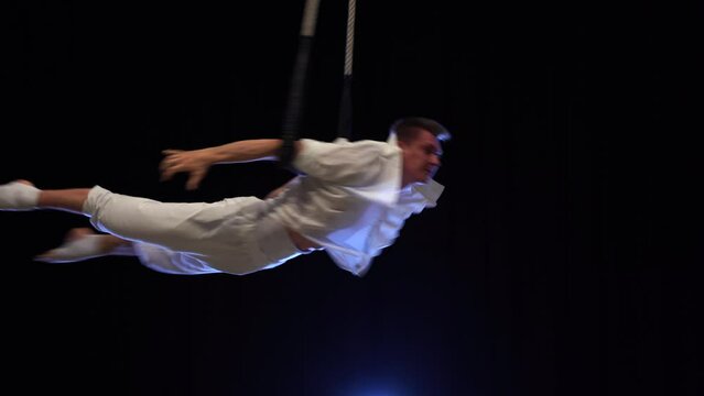 Muscular male aerial circus artist performances with dance trapeze. Movement and motion concept