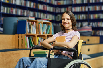 Vibrant portrait of young female student with disability looking at camera in college library and...