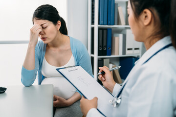 selective focus depressed pregnant mother is propping face in despair on desk while the female...