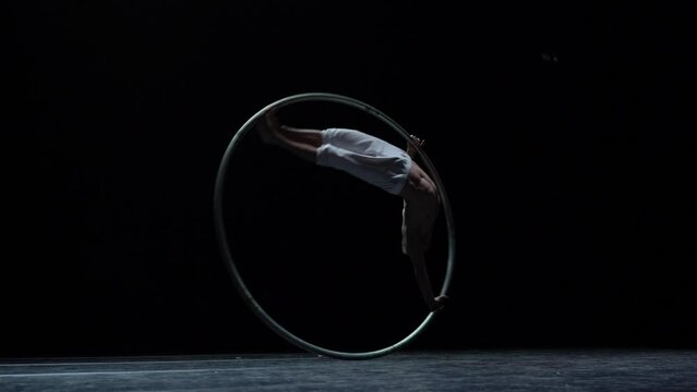 Muscular circus artist perform Cyr Wheel on a black background. Concept of originality, creativity and outstanding
