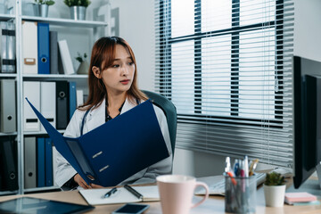 Taiwanese female medical worker sitting with a file folder in hands is looking outside the window...