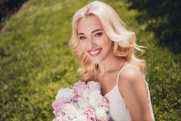 Fototapeta premium Photo of dreamy cute young curly girl dressed white singlet enjoying sunny weather holding bouquet outdoors countryside